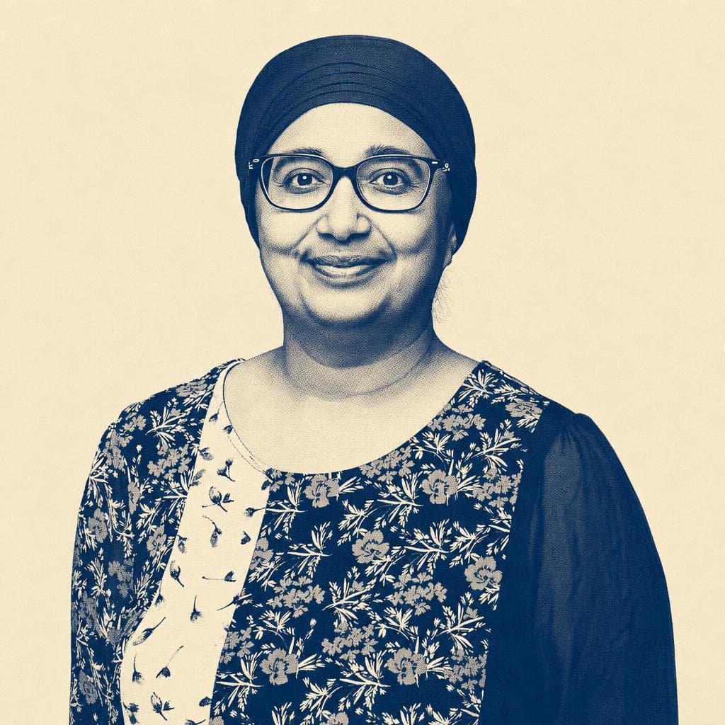 Balwinder Kaur, in a teal head covering and glasses, against a grey studio background.